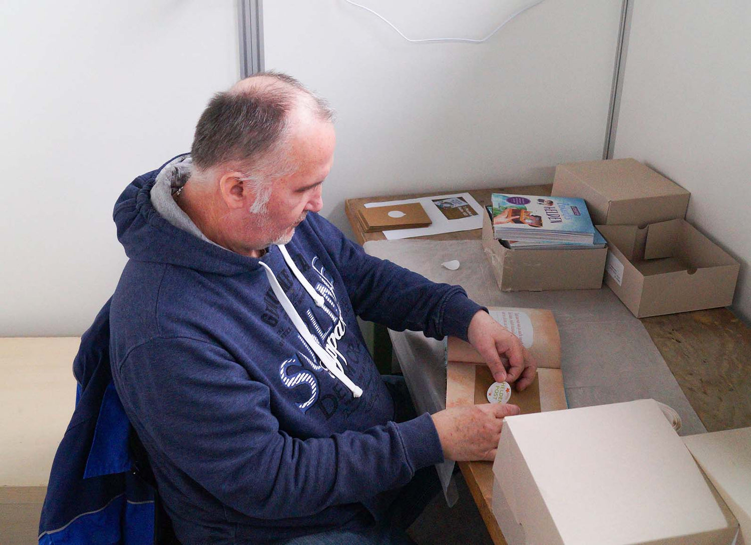 Partnerschaftliche Produktion: Ein Mitarbeiter der Werkstatt für Arbeitsförderung in Langenfeld verarbeitet unser "Zukunftshelden"-Buch und klebt wertvolle details, wie einen Sticker ein.